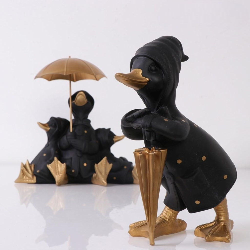 Μία όρθια μαύρη διακοσμητική πάπια με χρυσή ομπρέλα μπροστά από άλλες τρεις μαύρες πάπιες καθισμένες