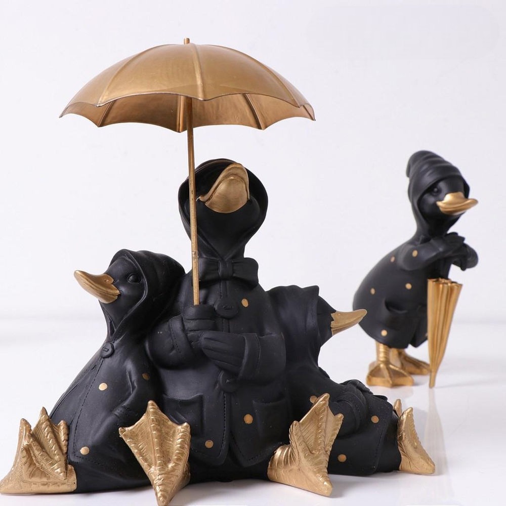 Τρεις καθιστές διακοσμητικές πάπια κάτω από μία ανοιγμένη χρυσή ομπρέλα