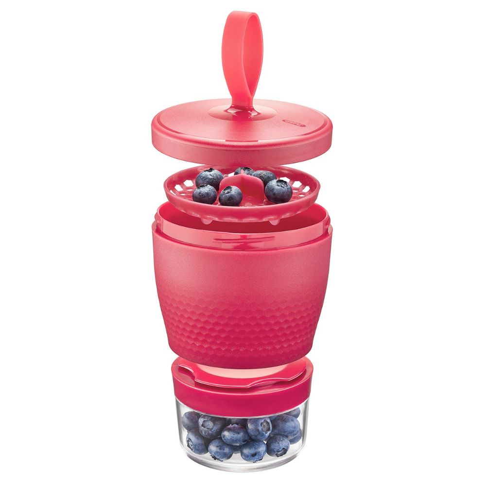 Ένα κόκκινο φαγητοδοχείο με διάφανη βάση γεμάτη με δημητριακά ανοιχτό και φρούτα στο πάνω μέρος